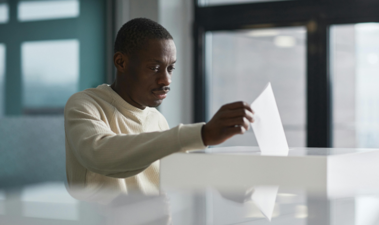 Abstimmen mit Behinderung Eine Person wirft einen Abstimmungszettel an der Urne ein.